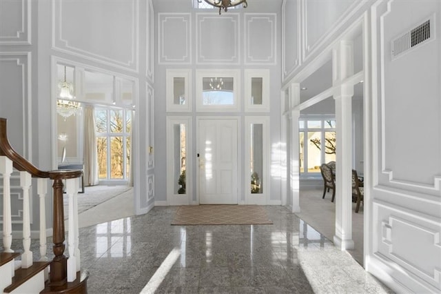 foyer entrance featuring a decorative wall, granite finish floor, a towering ceiling, visible vents, and an inviting chandelier