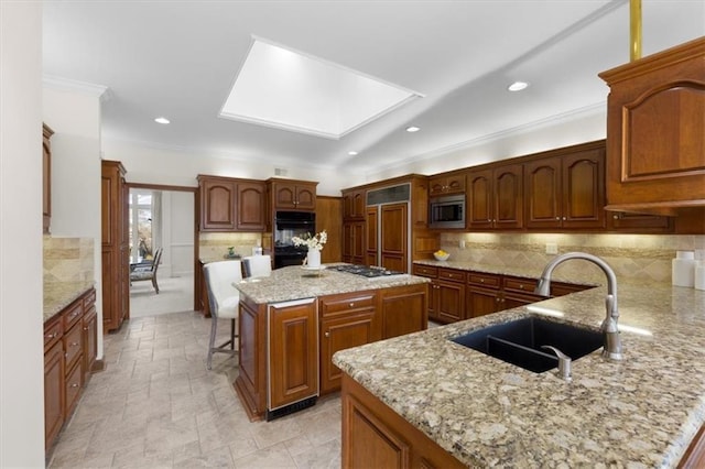 kitchen featuring built in appliances, light stone counters, a skylight, a sink, and tasteful backsplash