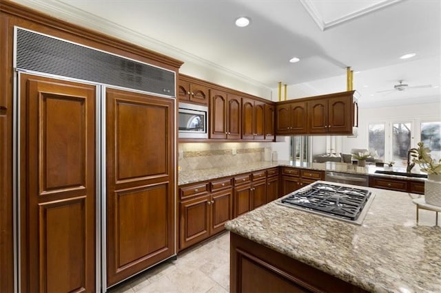 kitchen featuring light stone counters, recessed lighting, ornamental molding, a sink, and built in appliances