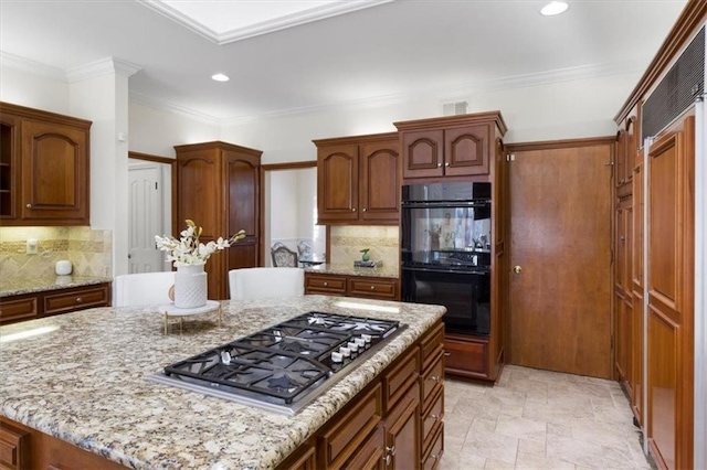 kitchen featuring light stone counters, a center island, dobule oven black, and stainless steel gas cooktop