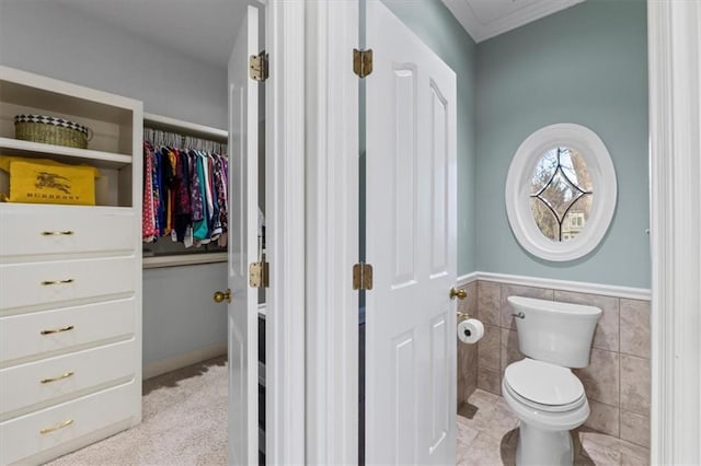 bathroom featuring toilet, a wainscoted wall, tile walls, a spacious closet, and tile patterned floors