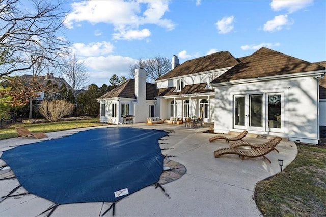 back of property featuring a covered pool, a patio, and a chimney