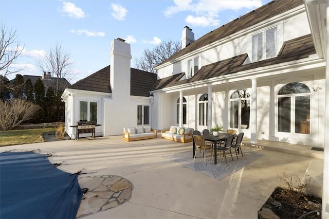 rear view of house with french doors, a chimney, stucco siding, a patio area, and an outdoor living space