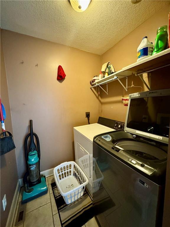 718 Oakland Ave, Kansas City, KS 66101 - clothes washing area with washing machine and dryer, a textured ceiling, laundry area, baseboards, and tile patterned floors