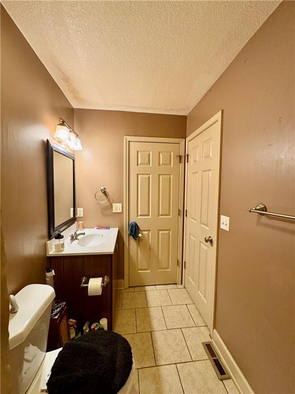 718 Oakland Ave, Kansas City, KS 66101 - half bathroom with visible vents, baseboards, toilet, tile patterned flooring, and vanity