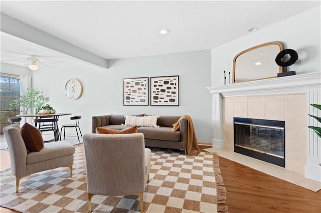 living room featuring a ceiling fan, a tiled fireplace, light wood-style flooring, and recessed lighting