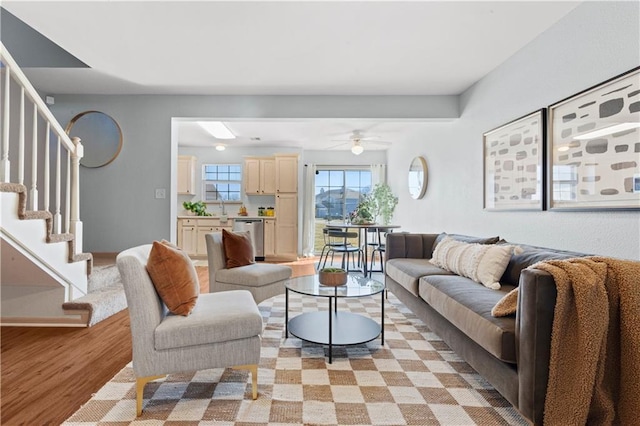 living area with light wood-style flooring, ceiling fan, and stairway