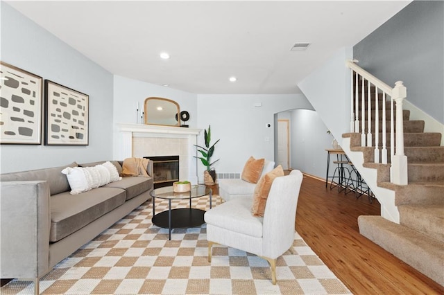 living room featuring arched walkways, a tile fireplace, recessed lighting, light wood-style floors, and stairs