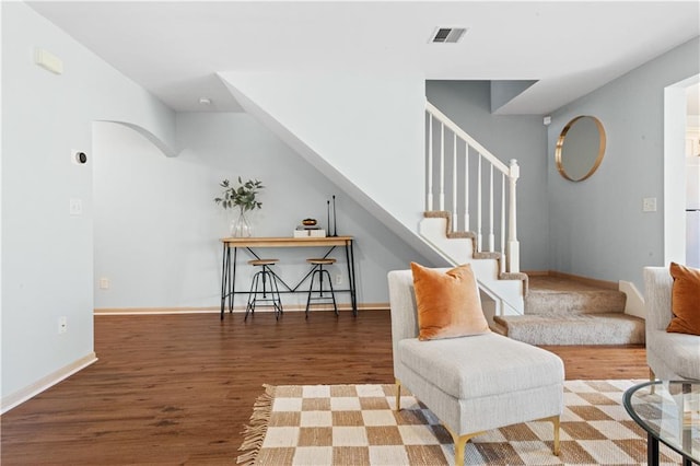 sitting room featuring arched walkways, visible vents, stairway, wood finished floors, and baseboards