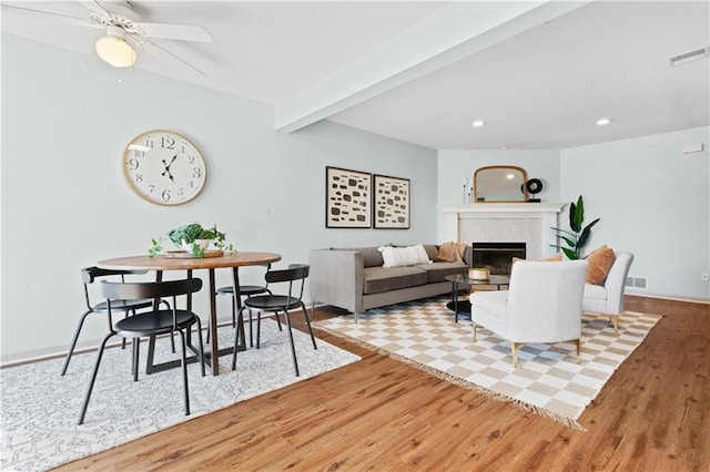 living area featuring light wood-type flooring, a glass covered fireplace, visible vents, and beamed ceiling