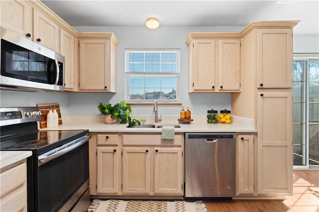 kitchen with appliances with stainless steel finishes, light countertops, a sink, and light brown cabinets