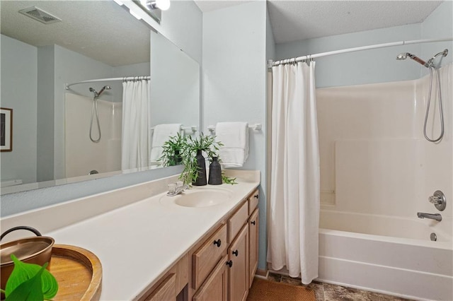 bathroom featuring double vanity, shower / bath combo, visible vents, a textured ceiling, and a sink