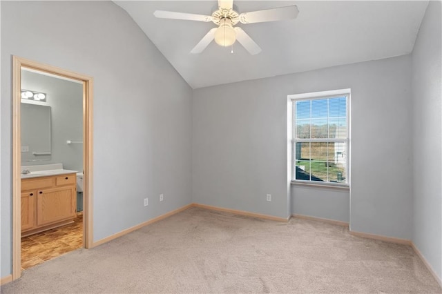 unfurnished bedroom featuring baseboards, a ceiling fan, light colored carpet, ensuite bath, and vaulted ceiling