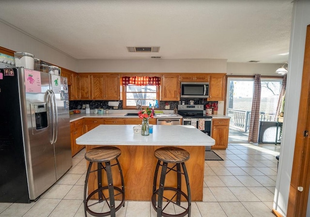 kitchen featuring light tile patterned floors, visible vents, appliances with stainless steel finishes, brown cabinets, and light countertops