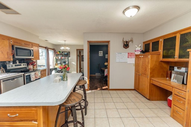 kitchen with visible vents, light countertops, appliances with stainless steel finishes, brown cabinetry, and a kitchen bar