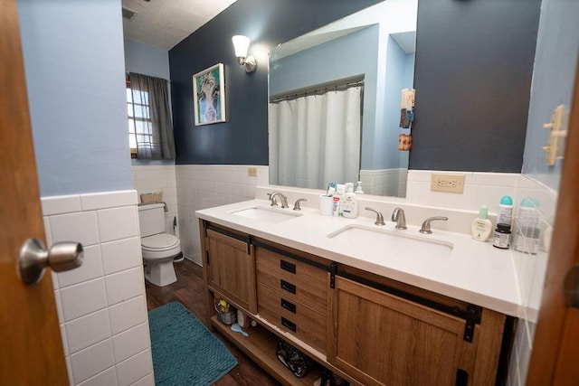 bathroom with toilet, a wainscoted wall, tile walls, and a sink