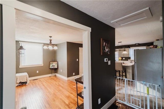 hallway with a textured ceiling, wood finished floors, visible vents, baseboards, and attic access