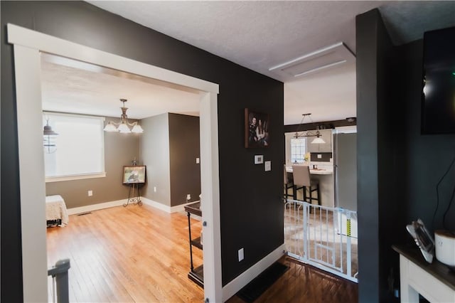 corridor with a chandelier, wood finished floors, visible vents, baseboards, and attic access