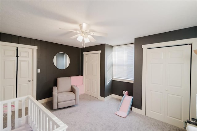 carpeted bedroom with ceiling fan, a crib, baseboards, and two closets