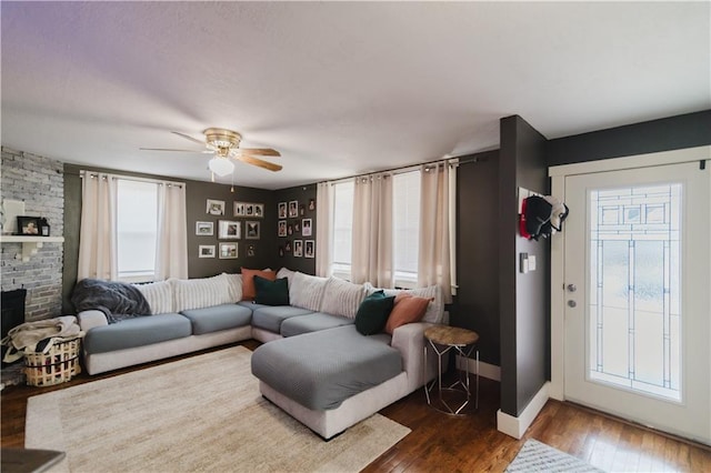 living area featuring dark wood-style floors, ceiling fan, a fireplace, and baseboards