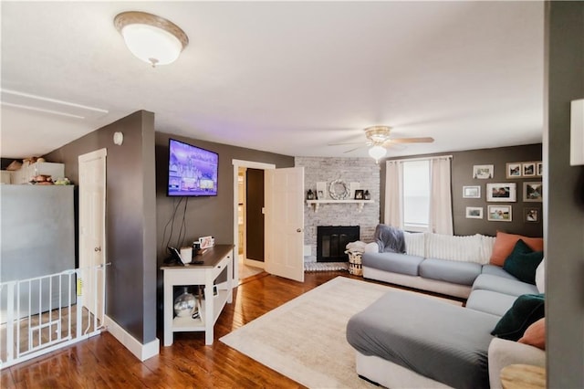 living room with dark wood-style floors, ceiling fan, a fireplace, and baseboards