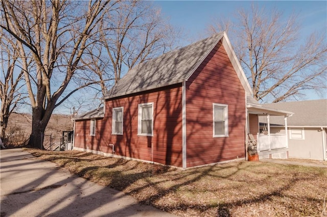 view of side of home featuring a shingled roof, a lawn, and a porch