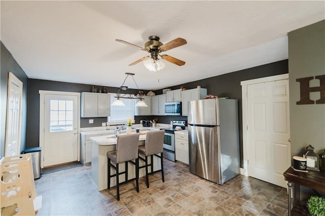 kitchen with a breakfast bar area, stainless steel appliances, white cabinets, light countertops, and a center island