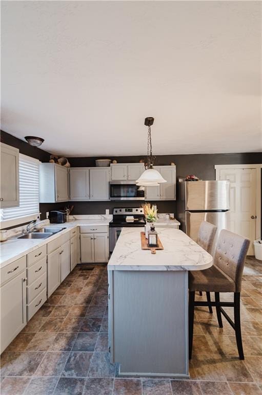 kitchen featuring stainless steel appliances, a sink, a kitchen island, stone finish floor, and decorative light fixtures