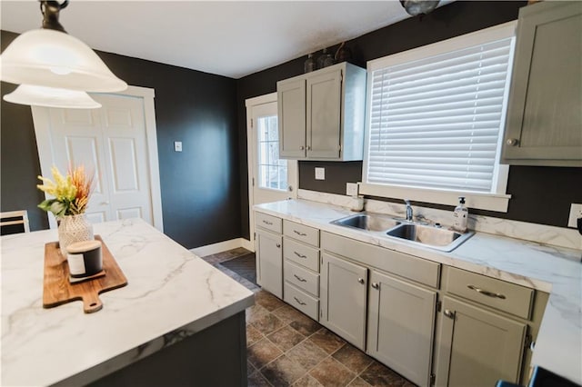 kitchen featuring stone finish flooring, baseboards, pendant lighting, and a sink