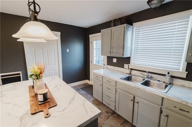 kitchen featuring hanging light fixtures, stone finish floor, a sink, light stone countertops, and baseboards