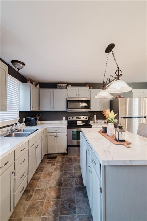 kitchen with a center island, pendant lighting, stainless steel appliances, stone finish floor, and a sink