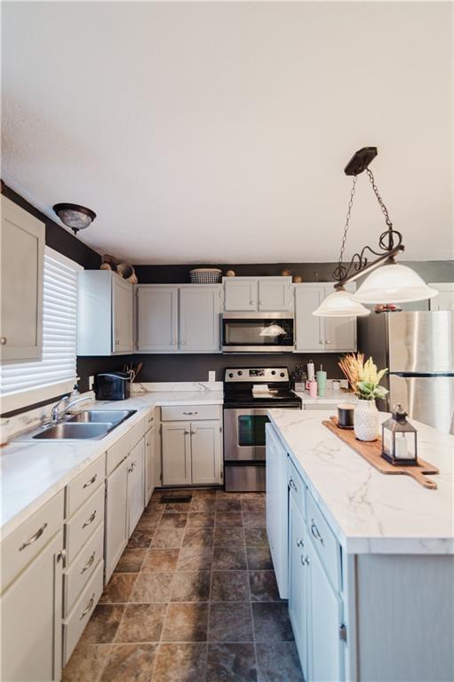 kitchen featuring a center island, pendant lighting, stainless steel appliances, stone finish flooring, and a sink