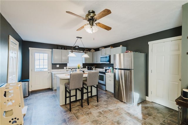 kitchen featuring a kitchen island, light countertops, appliances with stainless steel finishes, a kitchen bar, and decorative light fixtures