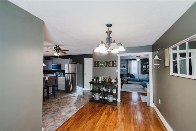 dining area with ceiling fan with notable chandelier, baseboards, and wood finished floors