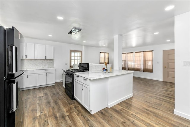 kitchen featuring white cabinets, dark wood-style floors, light stone countertops, black appliances, and backsplash