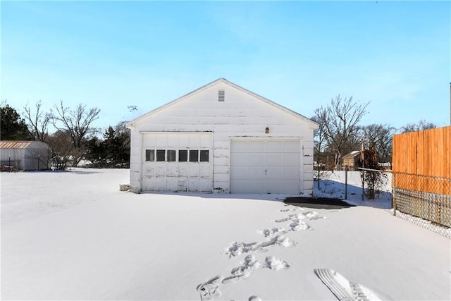 snow covered garage with a garage and fence