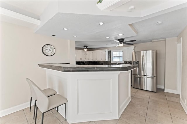 kitchen featuring tile countertops, a peninsula, white cabinets, stainless steel fridge with ice dispenser, and a kitchen bar