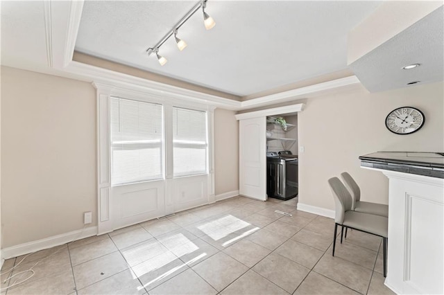 kitchen with light tile patterned floors, baseboards, rail lighting, a tray ceiling, and washing machine and dryer