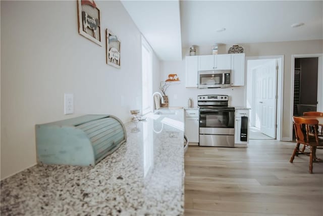 kitchen with stainless steel appliances, light wood-style flooring, white cabinets, a sink, and light stone countertops