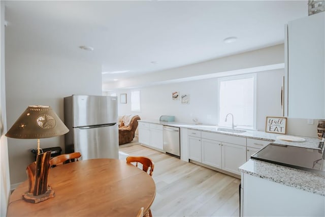 kitchen with white cabinets, freestanding refrigerator, light stone countertops, white dishwasher, and a sink