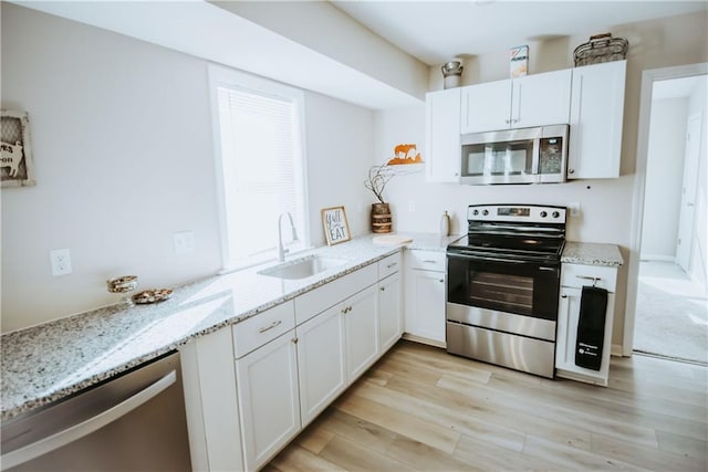 kitchen with light wood-style flooring, light stone countertops, stainless steel appliances, white cabinetry, and a sink