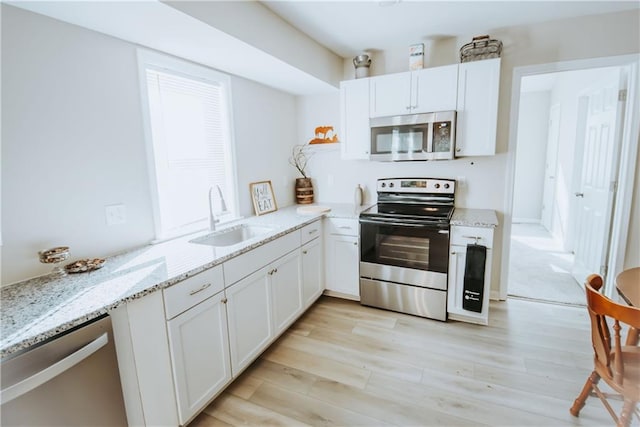 kitchen featuring light wood-style flooring, appliances with stainless steel finishes, light stone counters, white cabinetry, and a sink