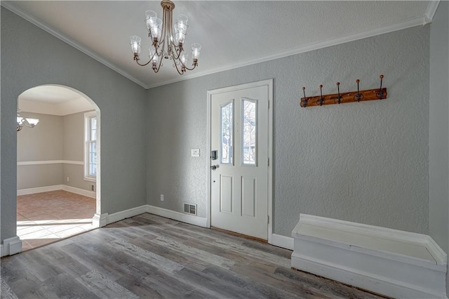 entrance foyer with wood finished floors, an inviting chandelier, arched walkways, ornamental molding, and a wealth of natural light