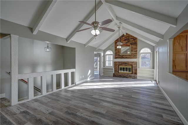 unfurnished living room with beamed ceiling, baseboards, wood finished floors, and a ceiling fan