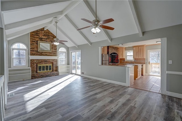 unfurnished living room with beam ceiling, a brick fireplace, a ceiling fan, and light wood-style flooring