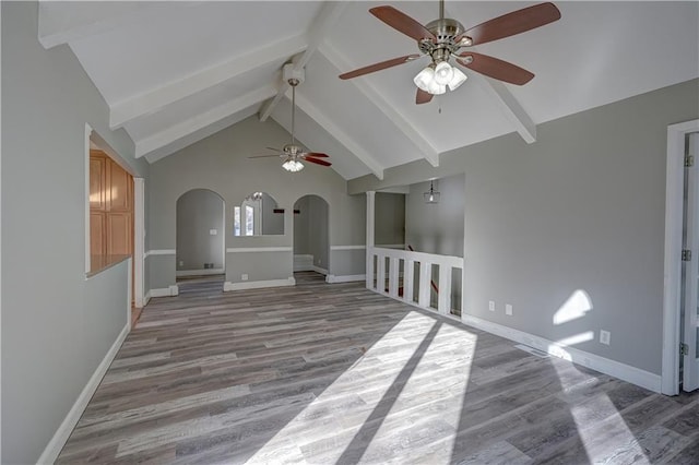 unfurnished living room with baseboards, ceiling fan, beam ceiling, wood finished floors, and arched walkways