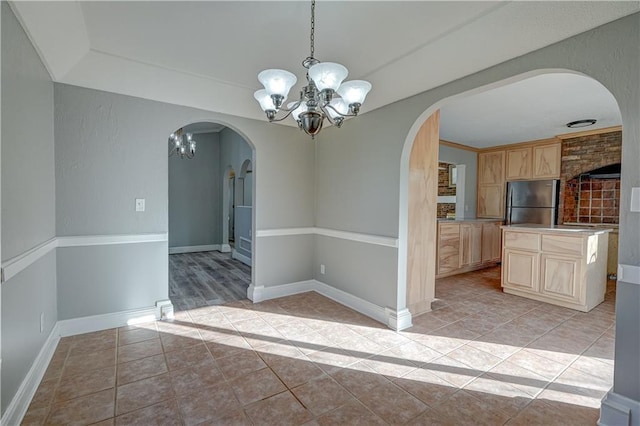 unfurnished dining area featuring a chandelier, light tile patterned floors, arched walkways, and baseboards