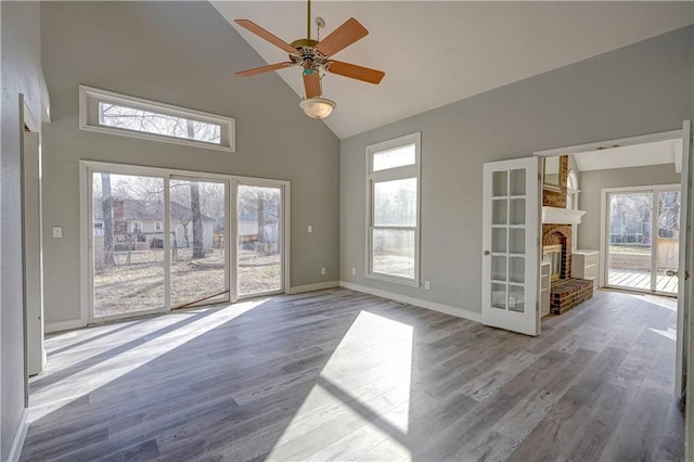 unfurnished room featuring high vaulted ceiling, a ceiling fan, wood finished floors, a fireplace, and baseboards