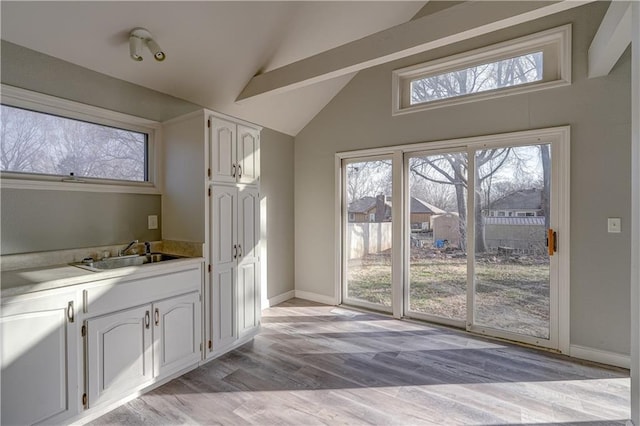 kitchen featuring light wood-style flooring, a sink, vaulted ceiling, white cabinets, and light countertops