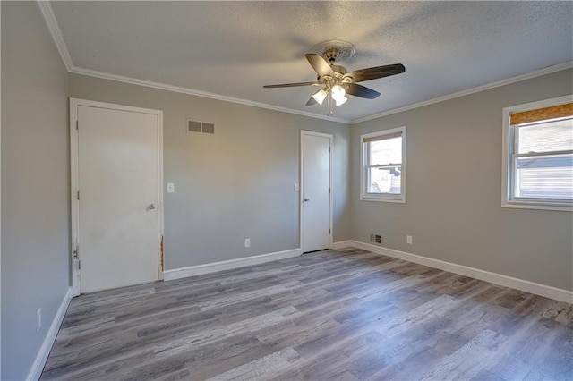 empty room featuring a ceiling fan, wood finished floors, visible vents, and ornamental molding